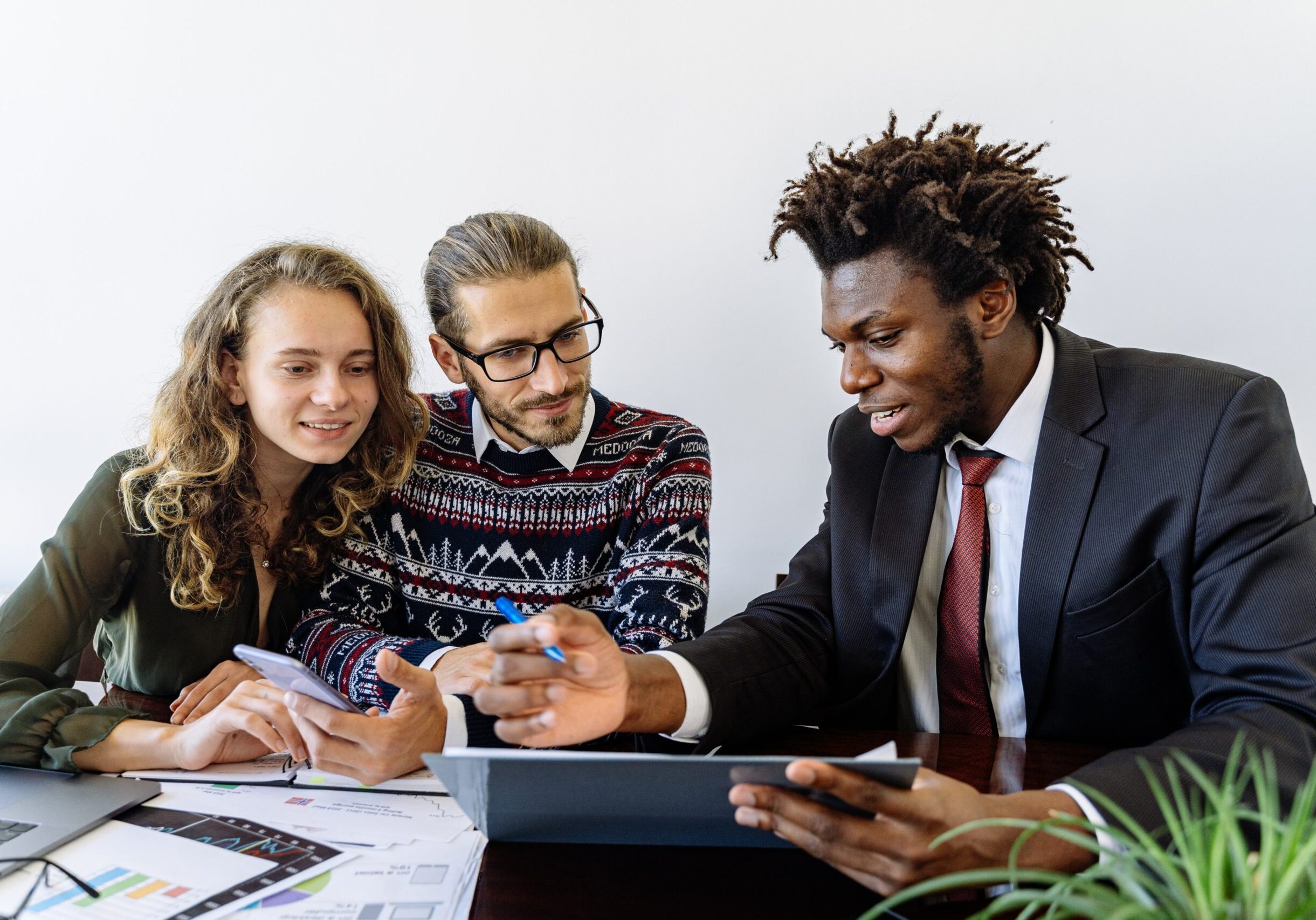 Three diverse professionals collaborating at a desk with documents and tablets while reviewing business materials.