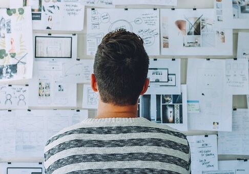 Person in striped shirt looking at wall covered in sketches, notes, and design documents from behind