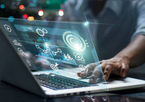 Person typing on laptop with holographic data visualizations and digital icons floating above screen in dark setting