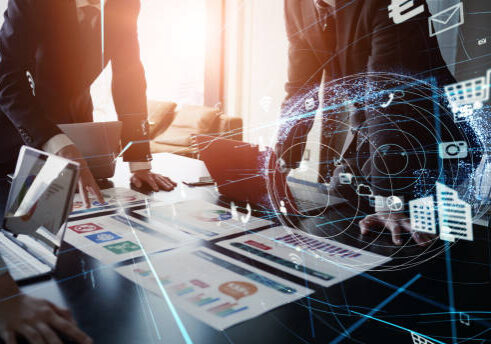 Business professionals analyze data charts and documents on a table with digital overlay of icons representing digital tools