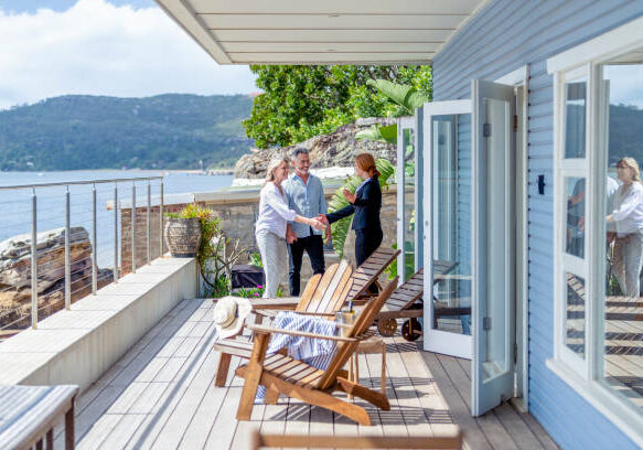 People meeting on a coastal deck of a blue beach house with Adirondack chairs and ocean views