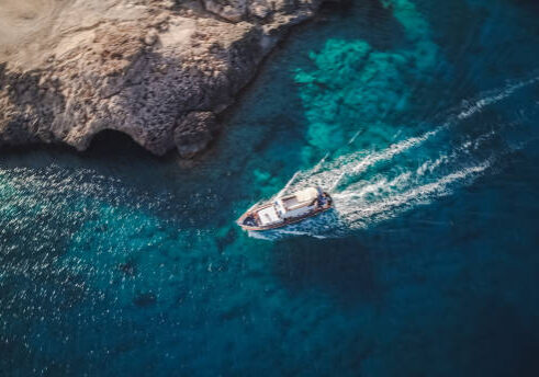 Aerial view of a yacht cruising through turquoise Mediterranean waters along a rocky coastline