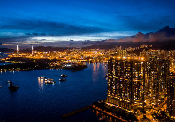 Illuminated Hong Kong skyline at night with glowing skyscrapers reflecting on harbor waters under a dramatic blue twilight sky