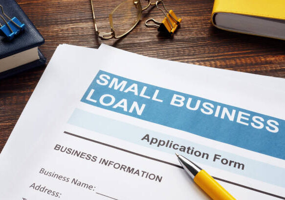 Small business loan application form on wooden desk with yellow pen, paper clips, and books