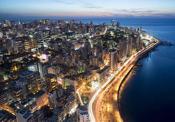 Aerial nighttime view of Beirut's coastline showing illuminated buildings and the curved Corniche waterfront along the Mediterranean Sea