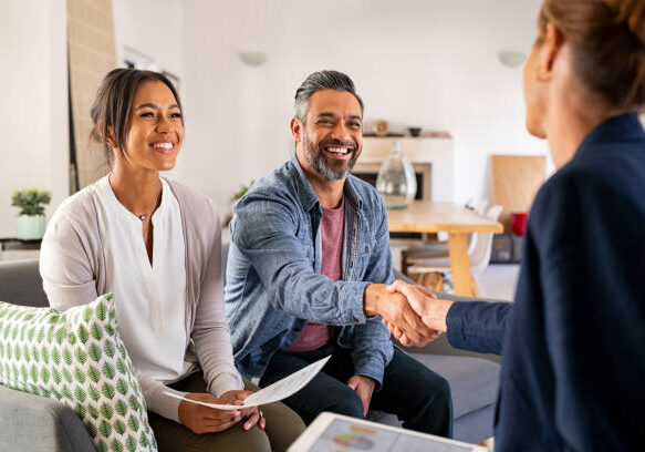 Couple meeting with financial advisor in living room, man shaking hands while woman smiles