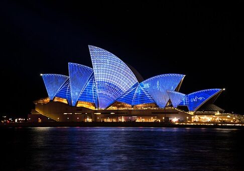 Sydney Opera House illuminated in blue lights at night, reflecting on harbor waters