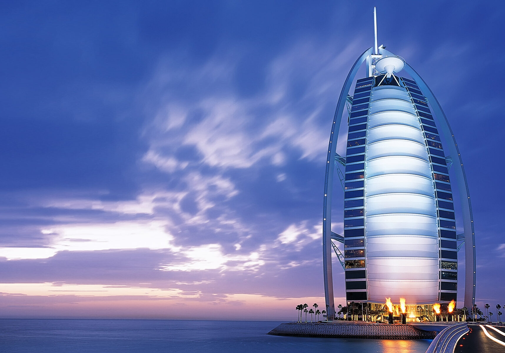 Burj Al Arab luxury hotel in Dubai at sunset, with its distinctive sail-shaped silhouette against a purple-blue sky over the ocean