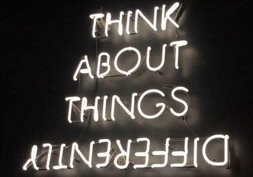 White neon sign reading 'THINK ABOUT THINGS DIFFERENTLY' with the last word upside down against a black background