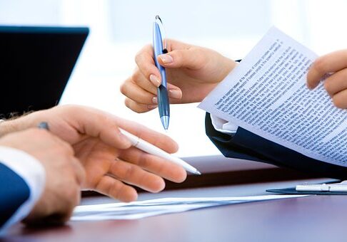 Close-up of hands reviewing and signing business documents with blue pens on a desk