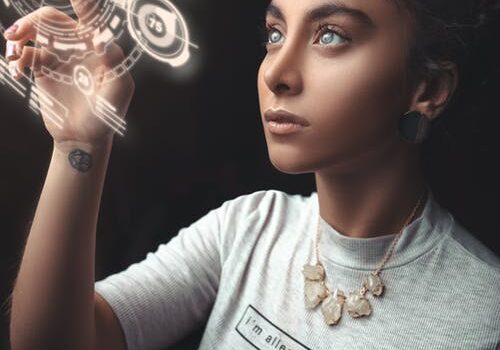 Woman in white t-shirt interacting with holographic tech interface displaying circular geometric patterns against dark background