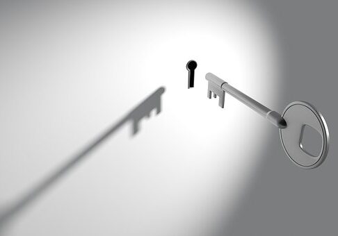 A silver key approaching a keyhole casting a long shadow against a gray background in a minimalist composition