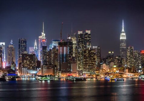 Manhattan skyline at night with illuminated skyscrapers including Empire State Building reflecting on Hudson River waters