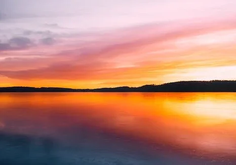 Vibrant sunset over a calm lake, with orange and pink skies reflecting perfectly on the mirror-like water surface