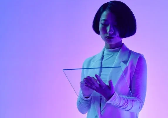 Professional woman in white blazer using transparent digital tablet under purple lighting in futuristic setting